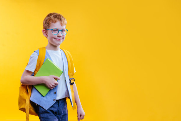 快乐的少年男孩拿着书包和书在黄色的背景图片下载