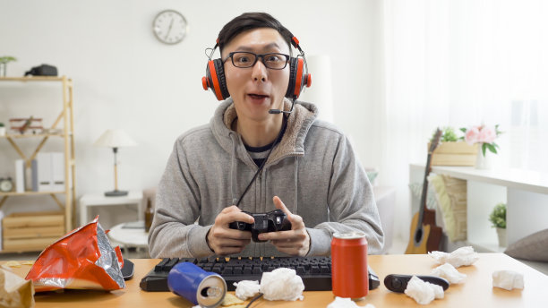 亚洲男子在网上游戏中意外获胜，他凝视着屏幕上的电脑。年轻英俊的男性家庭成员使用控制有乐趣在家里独自在暑假周末。图片下载