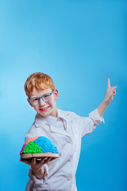 一名学生戴眼镜，穿着防护服，拿着蓝色背景上的大脑模型图片下载