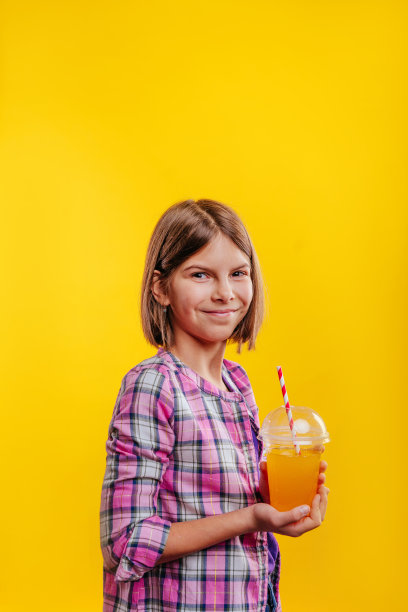 在黄色背景上喝橙汁的少女图片下载