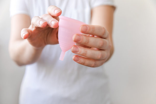 女人手拿粉红色月经杯白色背景隔离。女性月经期现代另类生态妇科卫生。女孩手上装血的容器图片下载