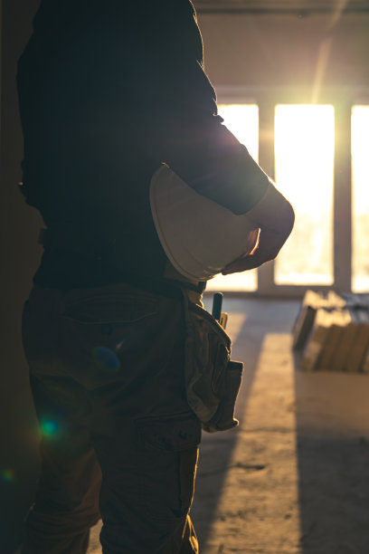 在建筑工地，一名手拿防护头盔的工人。图片下载