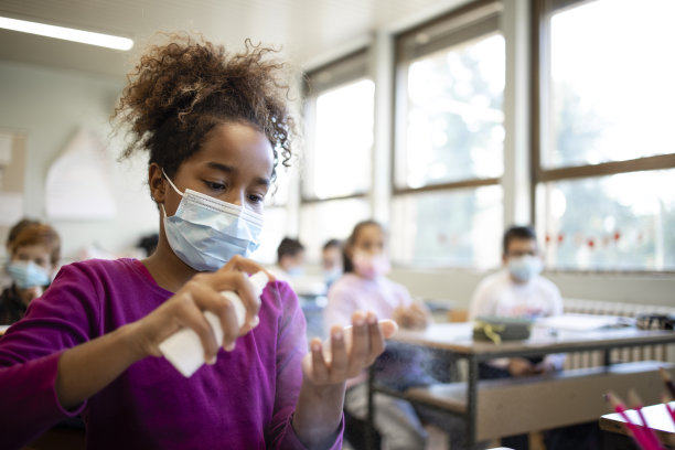 在冠状病毒大流行期间，学童戴口罩并在教室里消毒双手。图片下载