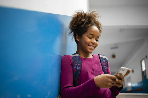 年轻的美国黑人女学生在学校走廊里用她的智能手机在社交网络上分享喜欢。图片下载