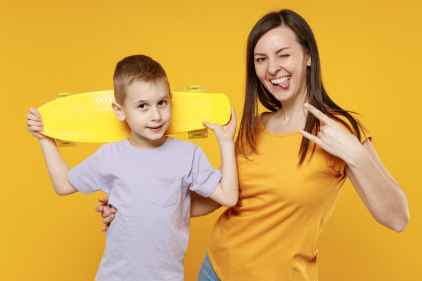 快乐年轻女人玩得开心孩子小男孩5-6-7岁身穿紫色t恤手持滑板妈妈抱着小男孩一起两个孤立在黄色背景工作室母亲节爱家庭概念。图片下载