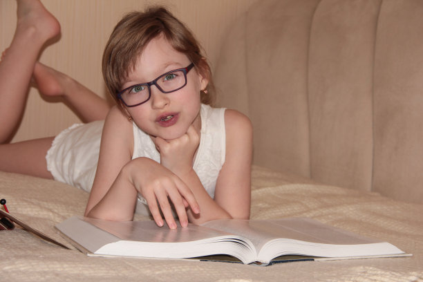 一个戴眼镜的孩子正躺在床上看书。远程学习。图片下载