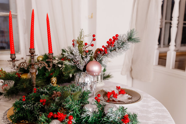 圣诞家庭餐桌概念。年夜饭的餐桌摆设。装饰品，蜡烛和灯笼。白色桌布。客厅装饰着彩灯和圣诞树。假期设置。圣诞红蜡烛图片下载