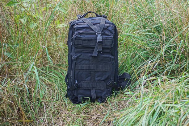 一个巨大的黑色战术背包站在绿色的草地上图片下载