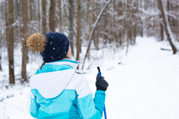 滑雪者在风衣和帽子绒球与滑雪杆在他的手与他的背对背景积雪的森林。冬季森林越野滑雪，户外运动，健康的生活方式。图片下载