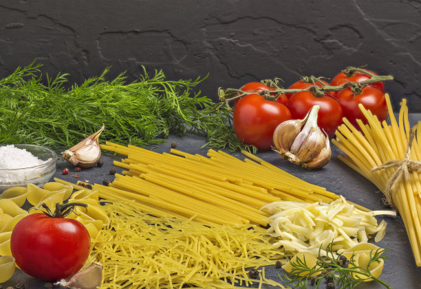 黑色背景的桌子上放着意大利面、红番茄、大蒜和香草图片下载