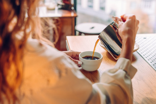 后视图的年轻女子坐在咖啡馆倒茶从茶壶图片下载