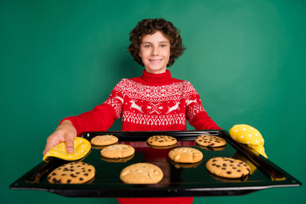 照片欢快的男孩展示托盘饼干穿鹿装饰毛衣孤立的绿色背景图片下载