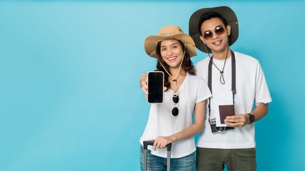 亚洲快乐的年轻夫妇游客准备旅行持有智能手机和行李复制空间孤立在蓝色横幅的背景。图片下载