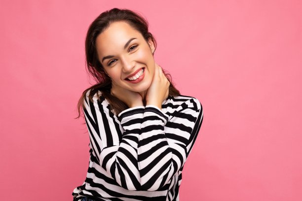 照片肖像年轻美丽的微笑嬉皮士黑发女人在时尚的套衫。性感无忧无虑的女性在工作室的粉红色墙壁附近摆着孤立的空空间。自然妆容的正面模特图片下载