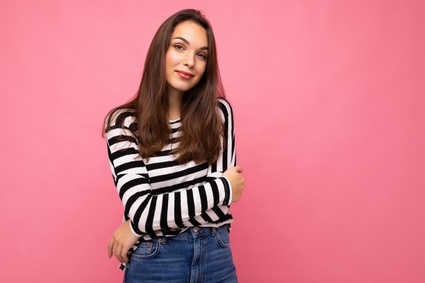 照片肖像年轻美丽的微笑嬉皮士黑发女人在时尚的套衫。性感无忧无虑的女性在工作室的粉红色墙壁附近摆着孤立的空空间。自然妆容的正面模特图片下载