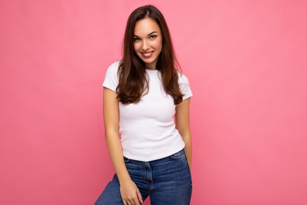 照片肖像年轻美丽的嬉皮士微笑黑发女人在白色t恤与模型。性感无忧无虑的女性在工作室的粉红色墙壁附近摆着孤立的空空间。自然妆容的正面模特图片下载