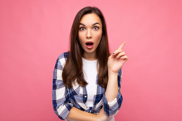 年轻美丽的黑发女人与真诚的情感穿着时尚的格子衬衫孤立在粉红色的背景与空白和有一个想法。哇概念图片下载