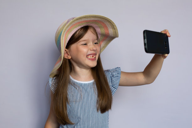 可爱的小女孩微笑着用智能手机自拍图片下载