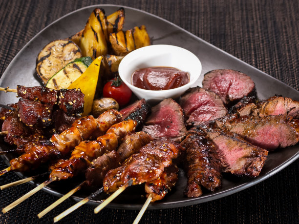 肉盘，一套不同的烤串和烤切片菲力牛排在盘子上与烤蔬菜，在黑暗的背景上近距离照片图片下载