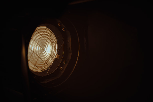 在黑暗的背景上，使用菲涅耳镜头的专业照明设备的特写。照片中的照明装置在左上方，在右下方发光。图片下载
