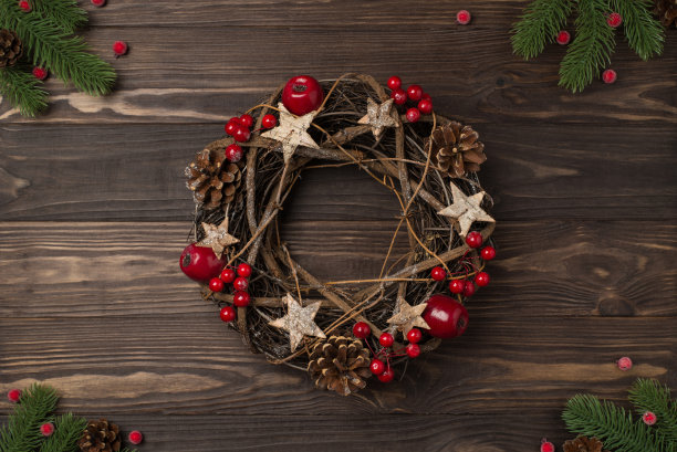 在孤立的深色木制书桌背景上的圣诞装饰松树树枝和小树枝花环与冬青浆果和松果的俯视图照片图片下载