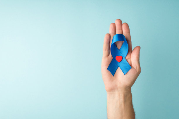 第一人称俯视照片的男性手拿蓝色丝带和小红心在手掌象征前列腺癌意识孤立的淡蓝色背景与空白图片下载