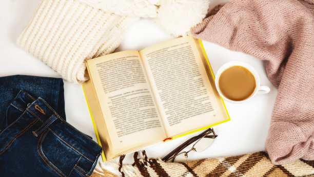 秋天的早晨咖啡。打开的书上放着一杯咖啡，白色的秋叶背景上放着暖和的衣服。静物的概念。副本的空间。图片下载