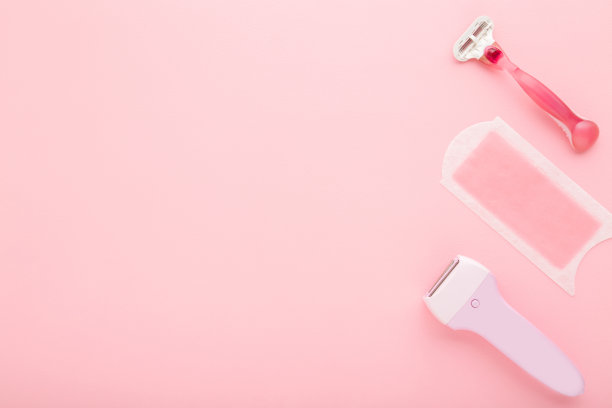 剃刀，蜡条和电脱毛器在浅粉红色的桌子背景。柔和的颜色。特写镜头。女性配件光滑的身体皮肤。为文本空出位置。自顶向下的观点。图片下载