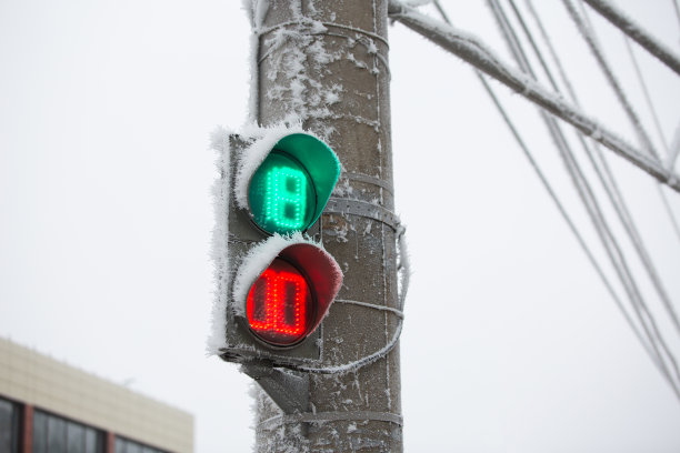 冰冻的红绿灯，背景是蓝天和电线。在冬天结冰的道路上事故的增加图片下载