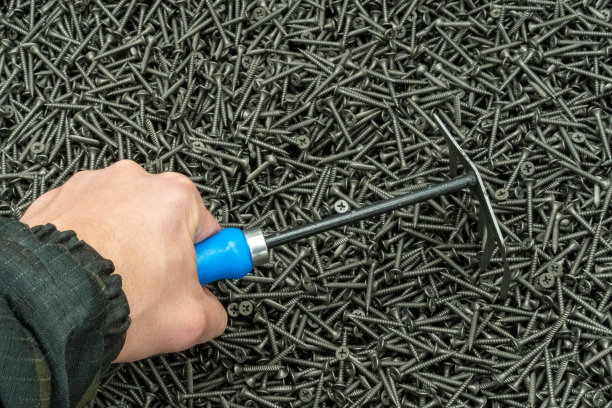 照片中的背景是钢螺钉和一个拿着耙子的男人的手。五金店图片下载