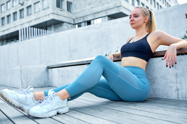 年轻的欧洲女性运动模特沿着城市背景在户外摆姿势，跑步，跳跃，慢跑，伸展，穿着运动紧身衣，运动鞋和黑色上衣图片下载