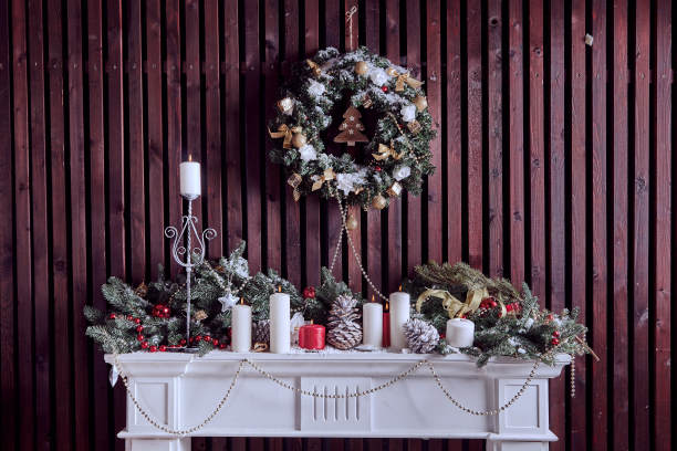 白色的圣诞架子上装饰着绿色的冷杉树枝、圆锥体、玩具、点燃的蜡烛和棕色木墙上的冷杉树枝花环图片下载