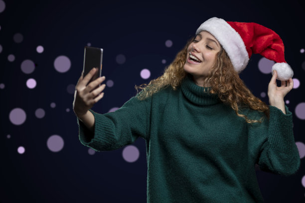 年轻的拉丁女子戴着圣诞帽，在无聚焦的灯光下快乐自拍图片下载