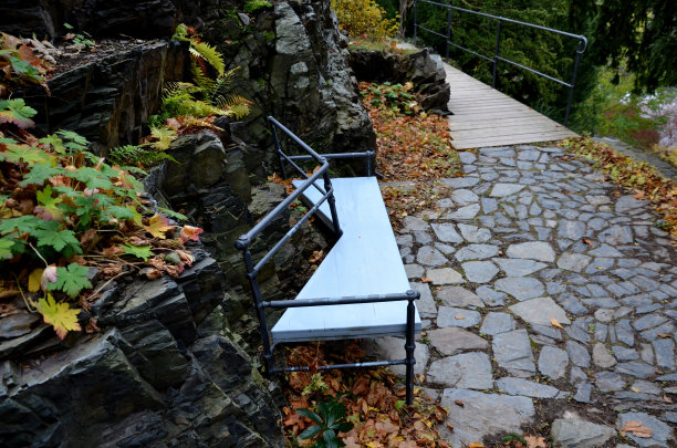 不规则几何多边形的木凳放在公园的石灰色路面上，低矮的挡土墙堆叠着斑岩。带有楼梯和自然岩石的观赏性花园图片下载