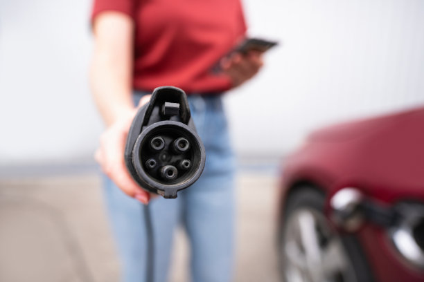 女人拿着智能手机展示电动汽车充电插头图片下载