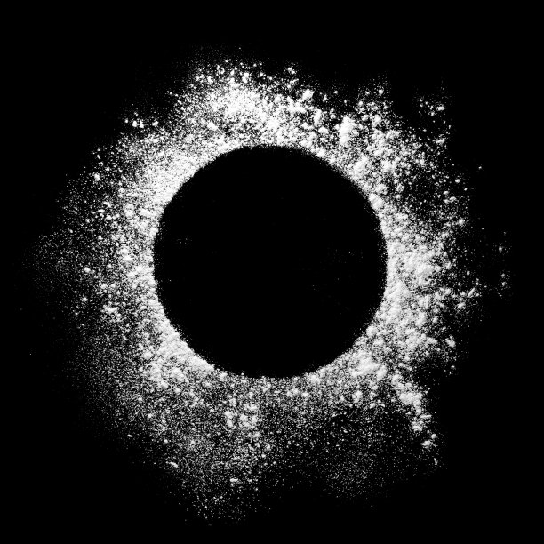 面粉从黑色桌子上的碗里撒出来。前视图。图片下载