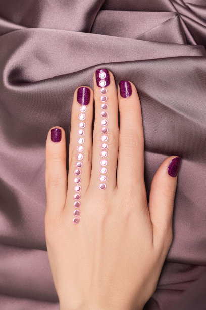 女性手与紫色指甲设计。闪闪发光的紫色指甲油指甲与宝石艺术。模特手和紫色的指甲。图片下载
