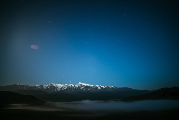 星空下，大雾弥漫，雪山连绵。在繁星点点的夜晚，阿尔卑斯山的风景是浓雾和大山脉。星空下的雪峰。图片下载