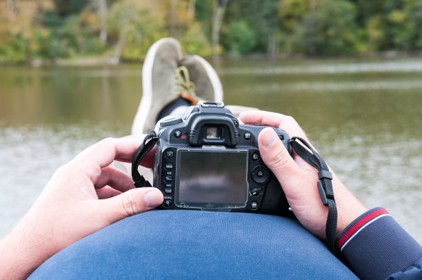 男人们的手拿着相机，背景是秋天有山的湖图片下载