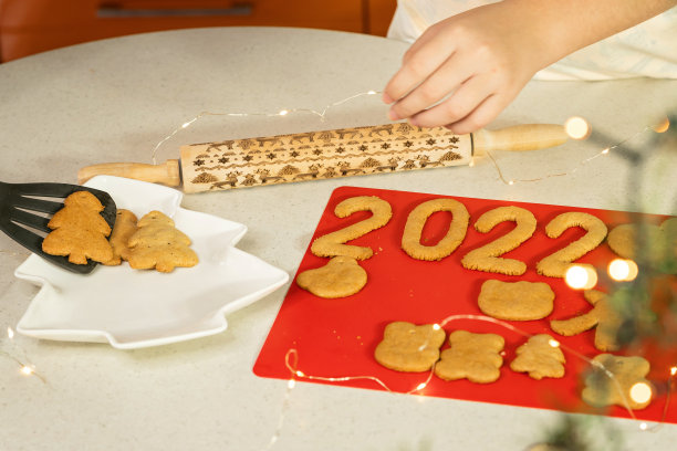 女人们用手把新做的姜饼饼干放进盘子里，做成圣诞树和数字2022图片下载