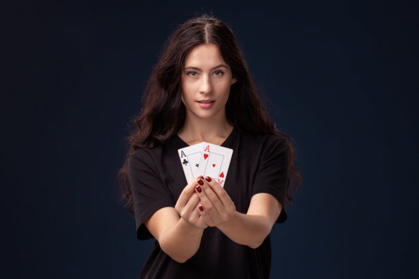 卷发的黑发女人手里拿着扑克牌摆造型。黑色背景上的扑克概念。赌场图片下载