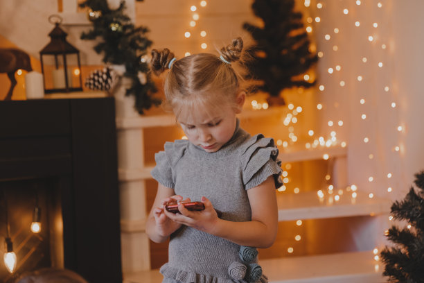 可爱的女孩在圣诞节的气氛中用智能手机说话，新年装饰的房子，孩子和现代科技，沟通的概念。图片下载