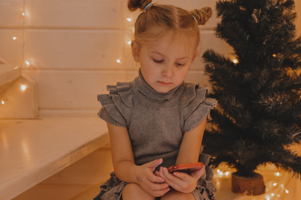 可爱的女孩在圣诞节的气氛中用智能手机说话，新年装饰的房子，孩子和现代科技，沟通的概念。图片下载