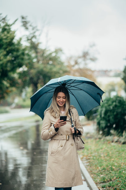 女商人打着雨伞，在下雨的时候用智能手机走在城市街道上图片下载