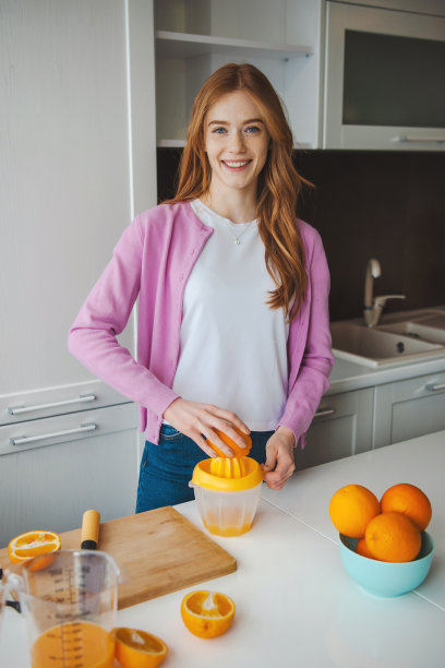 红头发、满脸雀斑的女人在厨房里榨汁。健康的饮食习惯图片下载