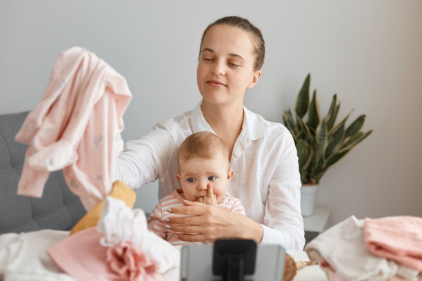 自信的年轻成年女性博主坐在三脚架上的手机前，录制童装销售视频，直播。图片下载
