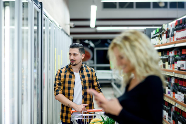一对夫妇在超市购物时使用智能手机和购物车图片下载