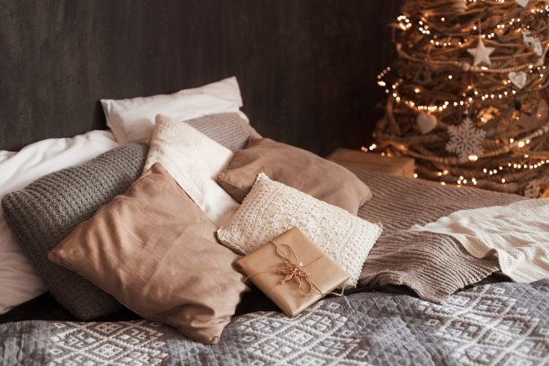 深色的时尚创意室内特写照片，大双人床上的许多枕头装饰着环保自制木制圣诞树和温暖的灯图片下载