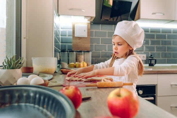 小女孩穿着围裙，戴着帽子，用擀面杖在桌子上揉面团图片下载