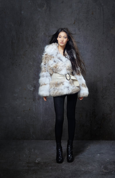 时尚的模特穿着人造毛皮大衣，风吹着头发，深色的内饰图片下载